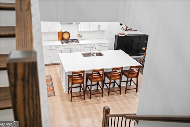 6045 Stargazer Way, Cumming, GA 30028 - kitchen with a sink, light wood-type flooring, white cabinetry, a breakfast bar, and stainless steel gas cooktop