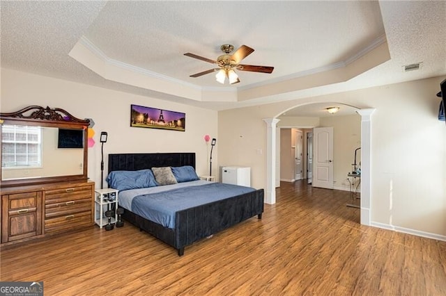 115 Pinnacle Ln, Mcdonough, GA 30253 - bedroom featuring decorative columns, a tray ceiling, crown molding, arched walkways, and light wood-style flooring