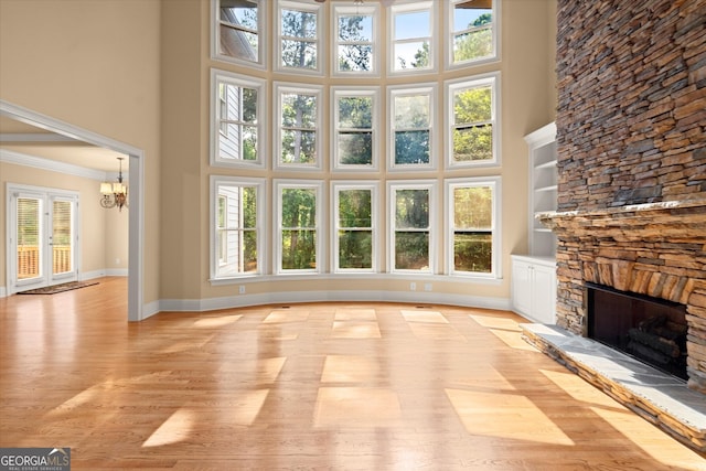 10565 Highgate Manor Ct, Duluth, GA 30097 - unfurnished living room featuring a towering ceiling, a stone fireplace, a chandelier, light wood-style floors, and baseboards