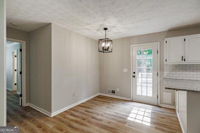 870 Rutherford Dr, Dacula, GA 30019 - unfurnished dining area with light wood-type flooring, a chandelier, and a textured ceiling