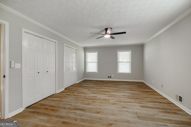 870 Rutherford Dr, Dacula, GA 30019 - unfurnished bedroom featuring multiple closets, light wood-style floors, crown molding, a textured ceiling, and ceiling fan