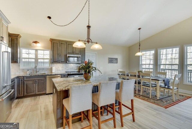 243 Degroff Ln, Rabun Gap, GA 30568 - kitchen featuring stainless steel appliances, vaulted ceiling, a breakfast bar area, tasteful backsplash, and light stone countertops