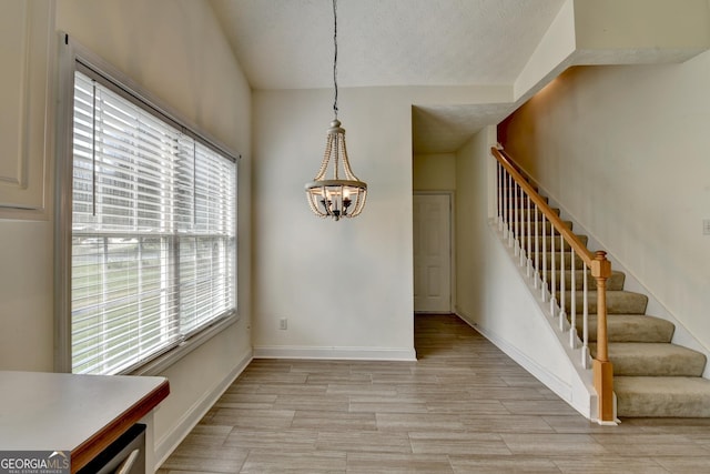2790 Meadow Gate Way, Loganville, GA 30052 - unfurnished dining area featuring a chandelier, stairs, light wood-type flooring, baseboards, and a textured ceiling