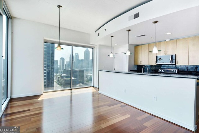 361 17th St NW Unit 1702, Atlanta, GA 30363 - kitchen with stainless steel microwave, dark countertops, light wood-style floors, tasteful backsplash, and light brown cabinets