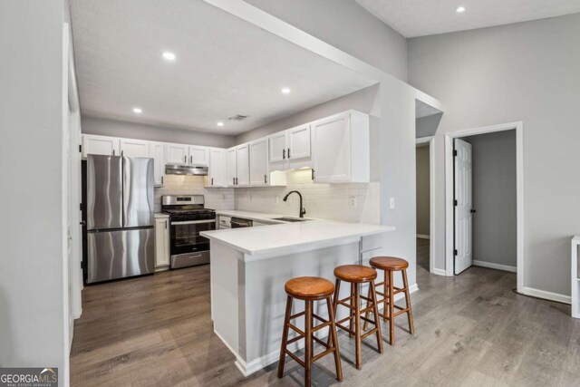 2657 Albion Farm Way, Duluth, GA 30097 - kitchen featuring stainless steel appliances, under cabinet range hood, a peninsula, tasteful backsplash, and wood finished floors
