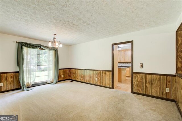 2612 Spring St, Dacula, GA 30019 - spare room with wooden walls, a wainscoted wall, a chandelier, light colored carpet, and a textured ceiling