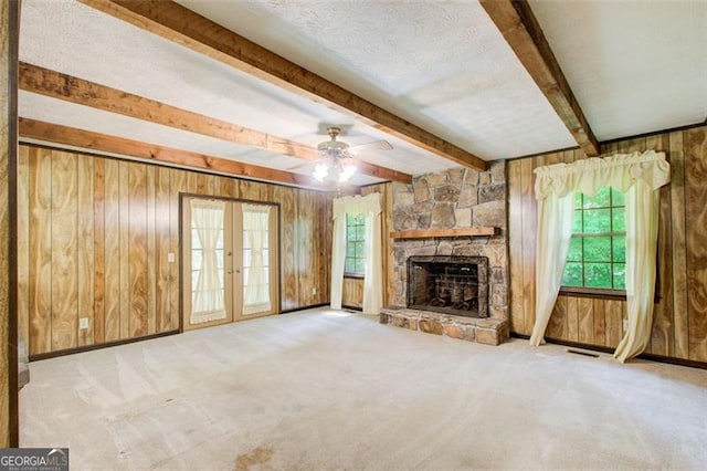 2612 Spring St, Dacula, GA 30019 - unfurnished living room with wood walls, french doors, a ceiling fan, a stone fireplace, and healthy amount of natural light