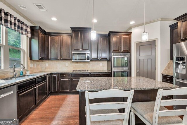 2525 Well Springs Dr, Buford, GA 30519 - kitchen featuring stainless steel appliances, ornamental molding, light stone countertops, a breakfast bar area, and dark brown cabinetry