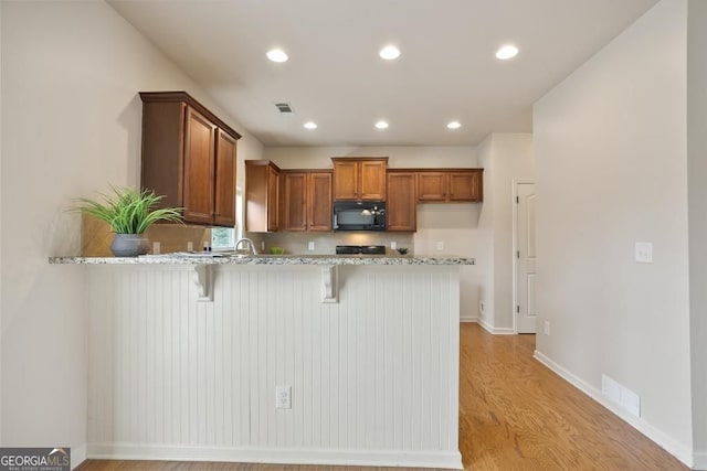 203 Creek View Ln, Acworth, GA 30102 - kitchen featuring black microwave, a peninsula, brown cabinetry, a kitchen bar, and light wood-style flooring