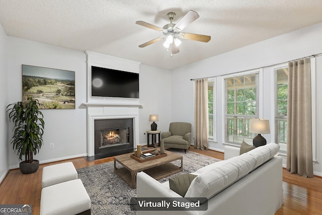 3850 Stepney Way, Cumming, GA 30041 - living area with a lit fireplace, a ceiling fan, wood finished floors, and a textured ceiling