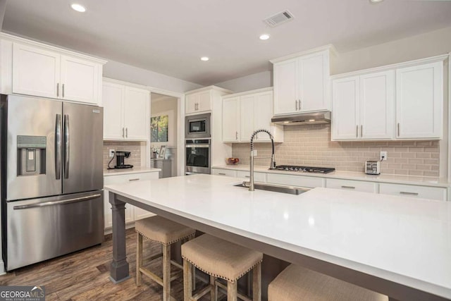 7345 Vale Ct, Cumming, GA 30028 - kitchen with appliances with stainless steel finishes, a sink, under cabinet range hood, decorative backsplash, and white cabinetry