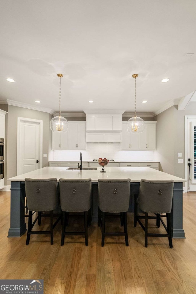 2377 Kesgrove Way, Buford, GA 30518 - kitchen with decorative backsplash, crown molding, a large island, light wood-type flooring, and white cabinetry