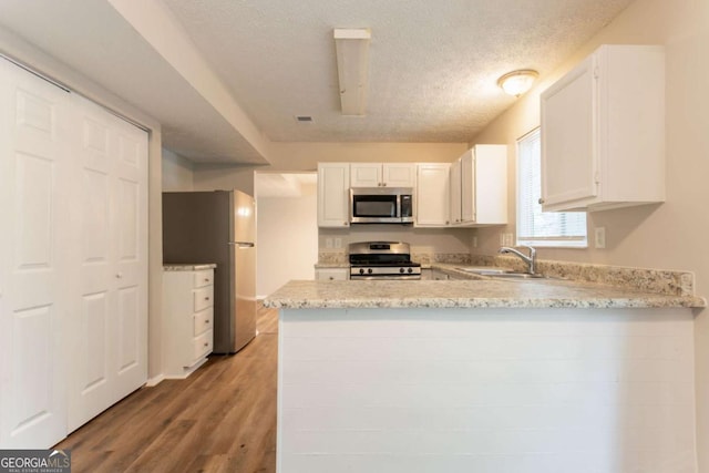 5092 Stone Trce, Stone Mountain, GA 30083 - kitchen featuring appliances with stainless steel finishes, a sink, a peninsula, a textured ceiling, and light wood-type flooring