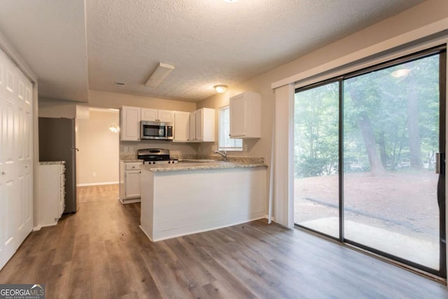 5092 Stone Trce, Stone Mountain, GA 30083 - kitchen with appliances with stainless steel finishes, a peninsula, white cabinetry, dark wood-style flooring, and a textured ceiling