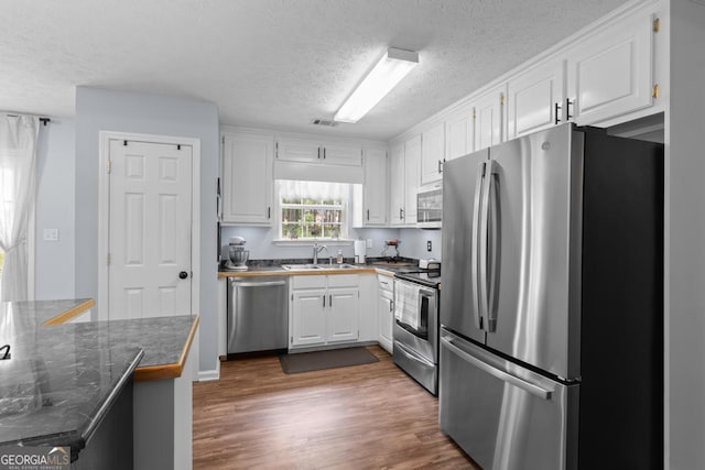 320 Cobb Ct, Hampton, GA 30228 - kitchen with appliances with stainless steel finishes, a sink, a textured ceiling, dark countertops, and white cabinetry