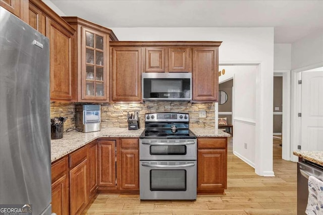 1637 Willow Way, Woodstock, GA 30188 - kitchen with appliances with stainless steel finishes, brown cabinets, decorative backsplash, light wood-style floors, and light stone countertops