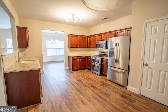 4135 Arch Pass, Cumming, GA 30040 - kitchen with appliances with stainless steel finishes, a chandelier, wood finished floors, light stone counters, and brown cabinets