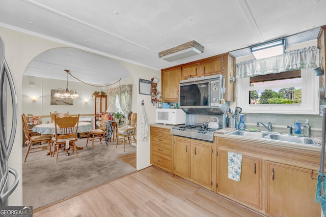 3131 Langley Rd, Loganville, GA 30052 - kitchen with appliances with stainless steel finishes, a sink, light wood finished floors, arched walkways, and hanging light fixtures