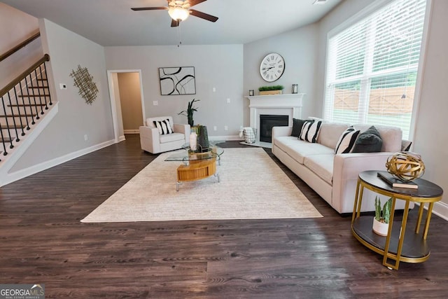 3557 Bryant Meadows Cir, Buford, GA 30519 - living room featuring a ceiling fan, stairs, dark wood-type flooring, a fireplace with flush hearth, and baseboards