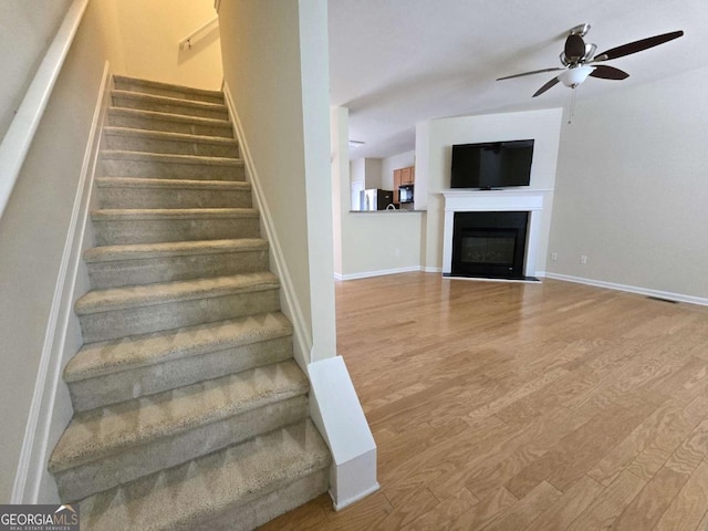 2104 Meadow Peak Rd, Duluth, GA 30097 - staircase featuring wood finished floors, a ceiling fan, and a fireplace with flush hearth