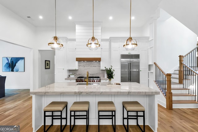 4235 Drew Campground Rd, Alpharetta, GA 30004 - kitchen featuring stainless steel built in refrigerator, backsplash, white cabinetry, light wood-style flooring, and a kitchen breakfast bar
