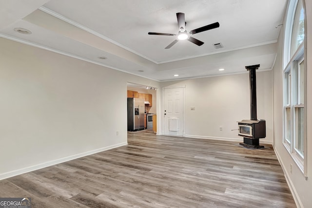 85 Prestigious Pl, Senoia, GA 30276 - unfurnished living room featuring a wood stove, a ceiling fan, light wood-type flooring, a raised ceiling, and ornamental molding