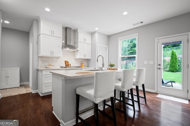 149 Archie Way, Woodstock, GA 30188 - kitchen featuring wall chimney exhaust hood, a sink, light countertops, dark wood finished floors, and a kitchen island with sink