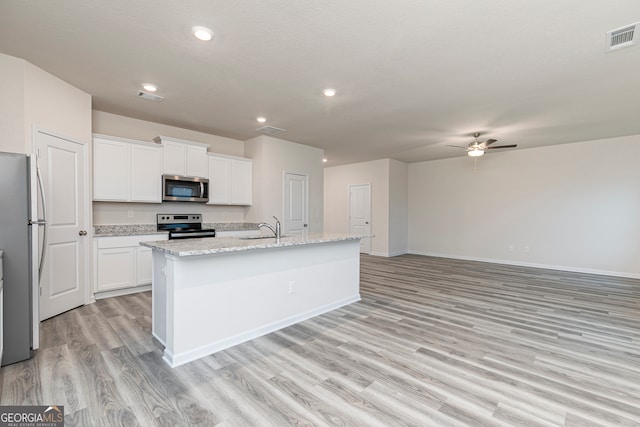 295 Limestone Cir, Conyers, GA 30013 - kitchen with stainless steel appliances, a sink, light wood finished floors, ceiling fan, and white cabinetry