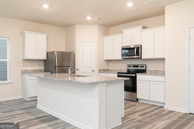 295 Limestone Cir, Conyers, GA 30013 - kitchen with appliances with stainless steel finishes, a sink, light wood finished floors, a center island with sink, and white cabinets
