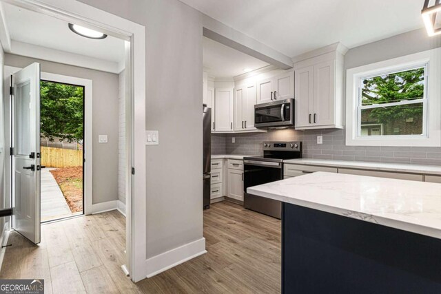 1283 Beecher St SW, Atlanta, GA 30310 - kitchen featuring appliances with stainless steel finishes, decorative backsplash, white cabinets, light wood-style flooring, and light stone countertops