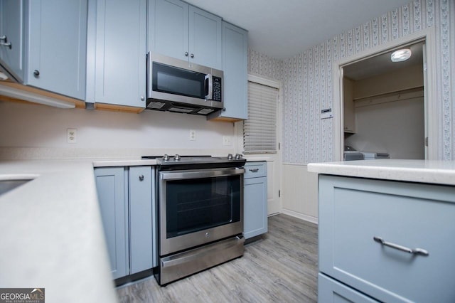 65 Pine Haven Ct, Carrollton, GA 30116 - kitchen with stainless steel appliances, wallpapered walls, a wainscoted wall, light countertops, and light wood-style flooring