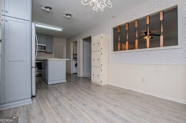 65 Pine Haven Ct, Carrollton, GA 30116 - kitchen with appliances with stainless steel finishes, wallpapered walls, light wood-style floors, wainscoting, and washer / clothes dryer