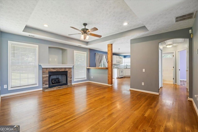 7825 Running Fox Trl, Gainesville, GA 30506 - unfurnished living room featuring a textured ceiling, ceiling fan, a raised ceiling, arched walkways, and wood finished floors