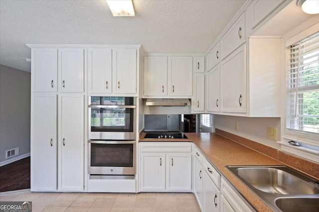 3802 Birchbriar Ct, Decatur, GA 30034 - kitchen with double oven, white cabinets, a textured ceiling, black electric cooktop, and under cabinet range hood