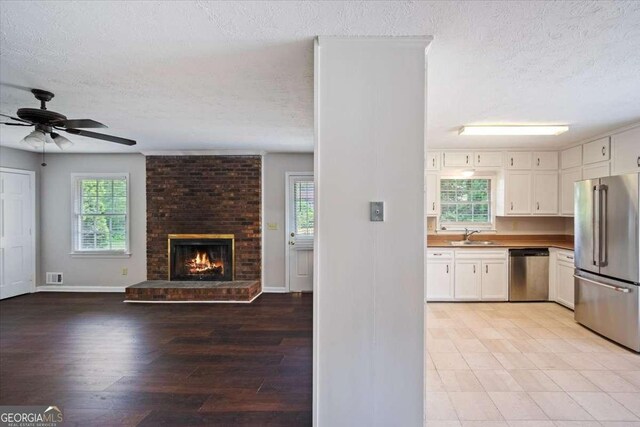 3802 Birchbriar Ct, Decatur, GA 30034 - unfurnished living room with a textured ceiling, baseboards, ceiling fan, a fireplace, and light wood-type flooring