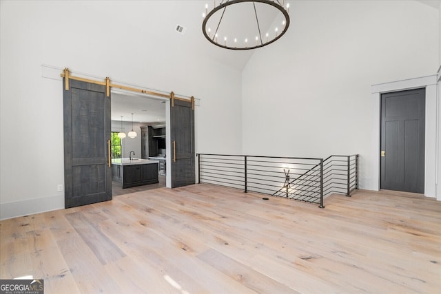 4927 Slaton Dr, Acworth, GA 30101 - unfurnished room with high vaulted ceiling, light wood-style flooring, a chandelier, and a barn door