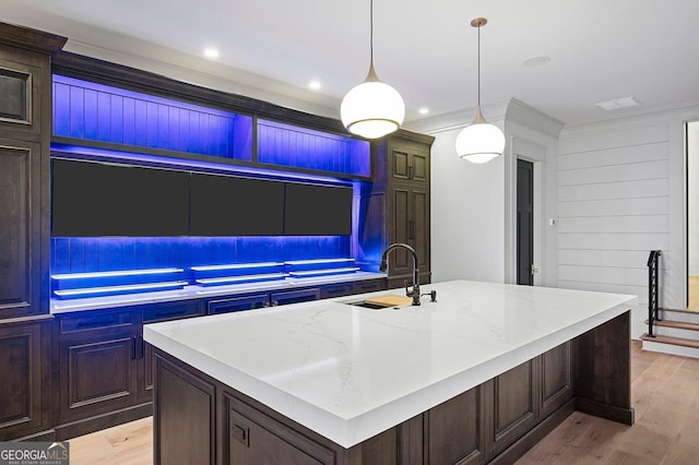 4927 Slaton Dr, Acworth, GA 30101 - kitchen featuring light wood-style flooring, a kitchen island with sink, light stone counters, hanging light fixtures, and crown molding