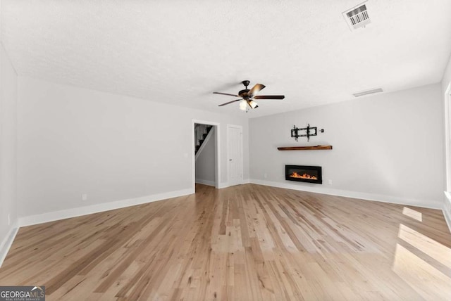 4690 Giddon Martin Rd, Gainesville, GA 30506 - unfurnished living room featuring a glass covered fireplace, light wood-style flooring, ceiling fan, baseboards, and a textured ceiling