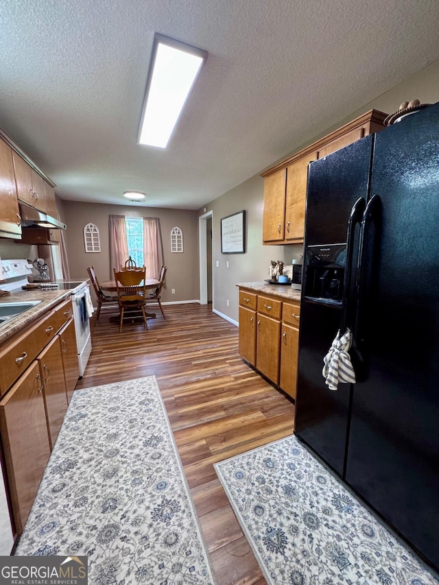 309 Ralph Wommack Rd, Hazlehurst, GA 31539 - kitchen featuring black fridge, electric stove, wood finished floors, under cabinet range hood, and light countertops