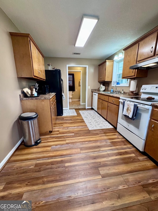 309 Ralph Wommack Rd, Hazlehurst, GA 31539 - kitchen with white appliances, under cabinet range hood, light wood-type flooring, baseboards, and brown cabinetry