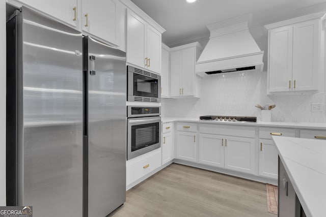 155 Lapis Lake Pt, Fayetteville, GA 30215 - kitchen featuring appliances with stainless steel finishes, custom range hood, white cabinetry, light wood-type flooring, and backsplash
