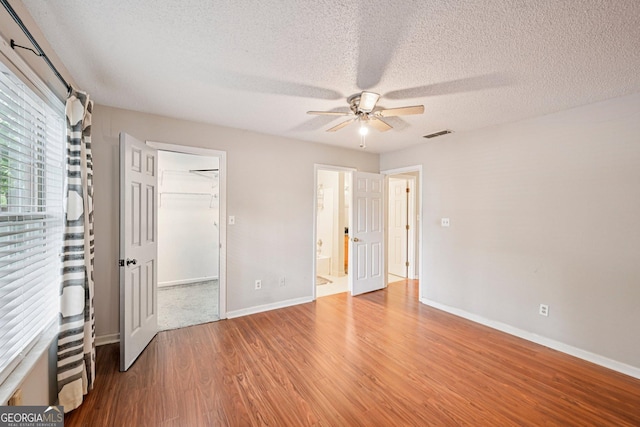 514 Mcgill Pl NE, Atlanta, GA 30312 - unfurnished bedroom featuring wood finished floors, a textured ceiling, baseboards, a ceiling fan, and a walk in closet