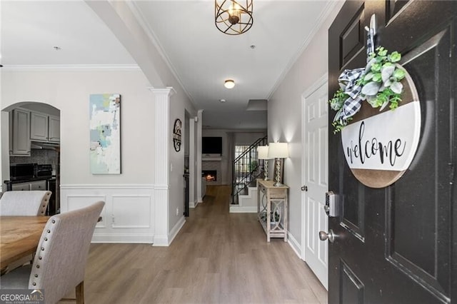 3088 Steeplechase Dr, Alpharetta, GA 30004 - entryway featuring ornamental molding, light wood finished floors, stairs, arched walkways, and a lit fireplace