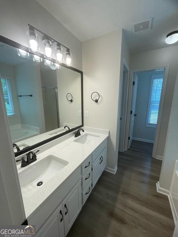 140 Clover Valley Dr, Covington, GA 30016 - bathroom featuring a bath, a shower stall, double vanity, wood finished floors, and baseboards