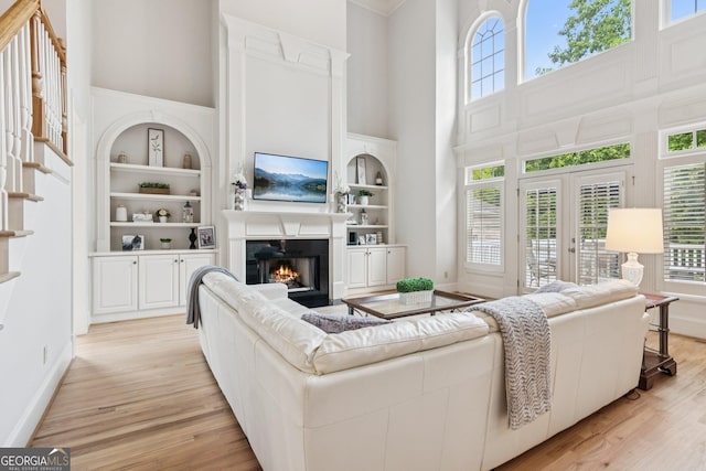 952 Moores Walk Ln, Suwanee, GA 30024 - living area featuring a high ceiling, light wood-style floors, a glass covered fireplace, french doors, and built in features