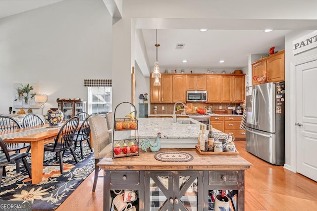 7891 Brass Lantern Dr, Flowery Branch, GA 30542 - kitchen with appliances with stainless steel finishes, light wood-style flooring, light stone counters, backsplash, and pendant lighting