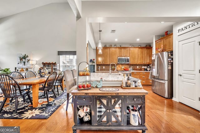 7891 Brass Lantern Dr, Flowery Branch, GA 30542 - kitchen featuring stainless steel appliances, light wood-type flooring, tasteful backsplash, light stone countertops, and brown cabinets