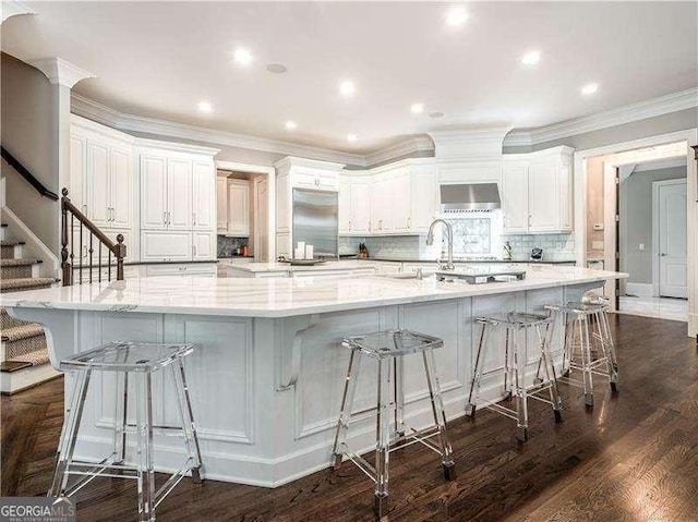 8957 Old Southwick Pass, Johns Creek, GA 30022 - kitchen featuring wall chimney range hood, dark wood-type flooring, a spacious island, tasteful backsplash, and crown molding