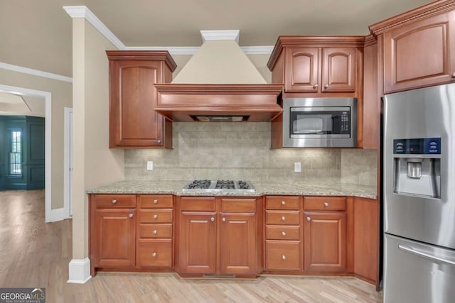 3451 Falls Branch Ct, Buford, GA 30519 - kitchen with stainless steel appliances, custom exhaust hood, light stone counters, light wood-style floors, and crown molding