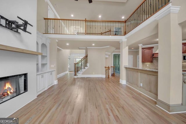 3451 Falls Branch Ct, Buford, GA 30519 - unfurnished living room with a towering ceiling, light wood-style floors, a lit fireplace, recessed lighting, and stairway